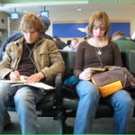 two twenty or so year olds sitting in airport on phones