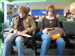 two twenty or so year olds sitting in airport on phones