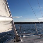 front of small sailboat heading towards land in distance