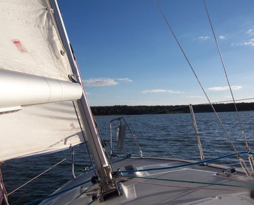 front of small sailboat heading towards land in distance