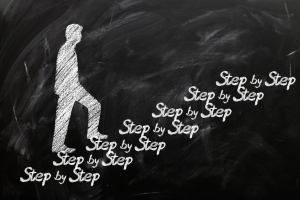 silhouette of a man walking up hand written steps that reads Step by Setp